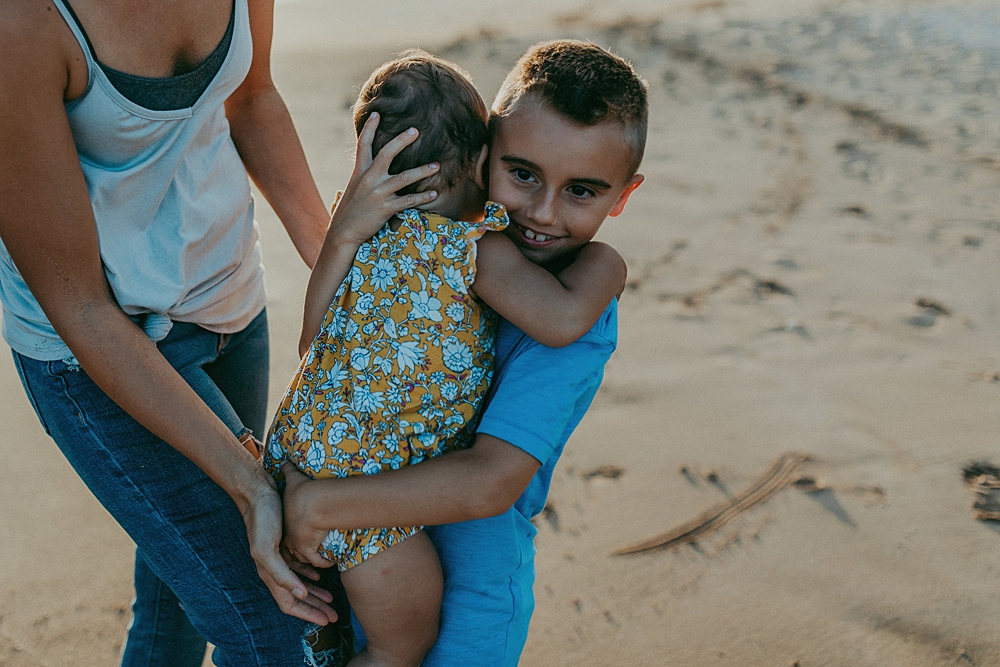Boy holds his foster sibling on the beach in Hawaii. 